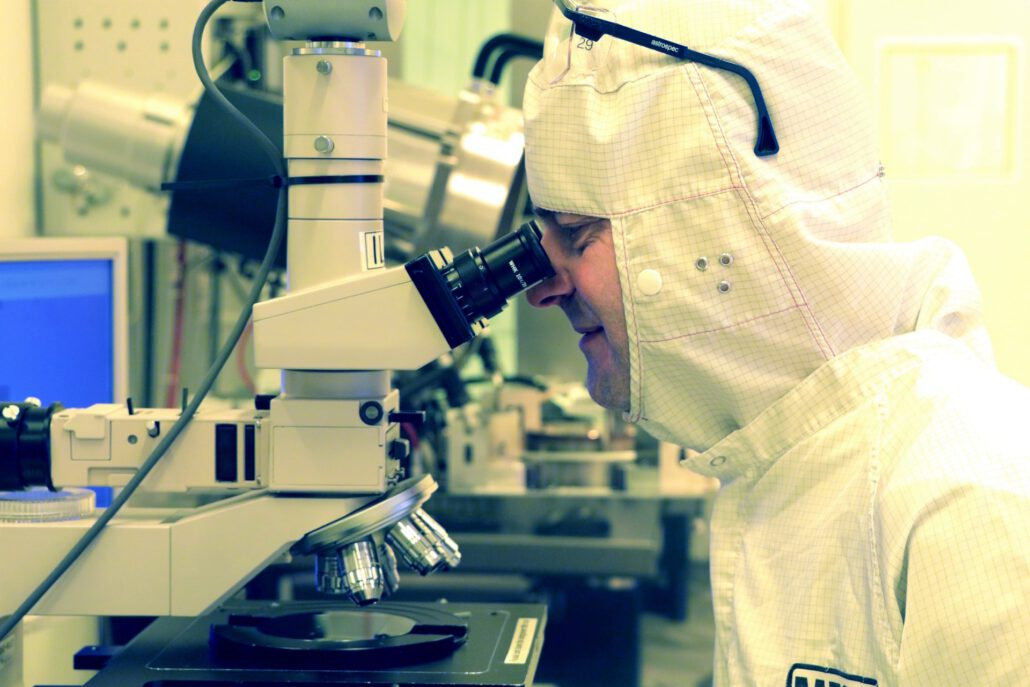 An engineer using a microscope to examine a MEMS chip wafer as part of MEMS development